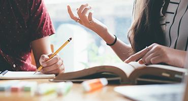 Two people studying, close up on hands and books on table