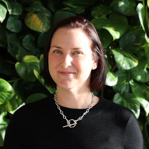 Jennifer Stanton, a woman with dark hair, sits against a leafy green background